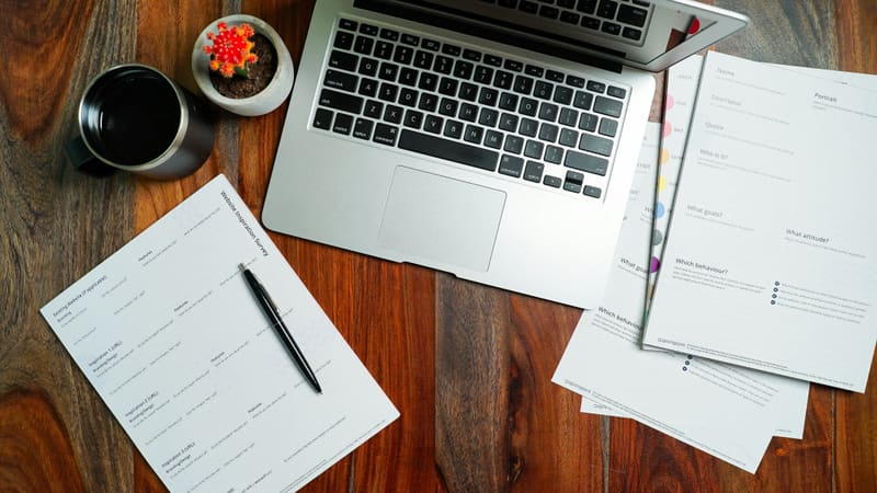 Laptop with printed forms, pen, and coffee on a desk