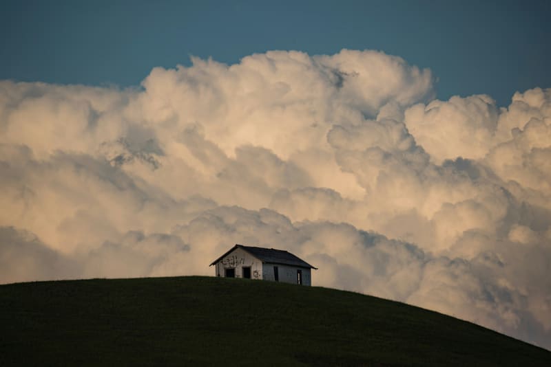 Lone house on a hilltop beneath massive clouds