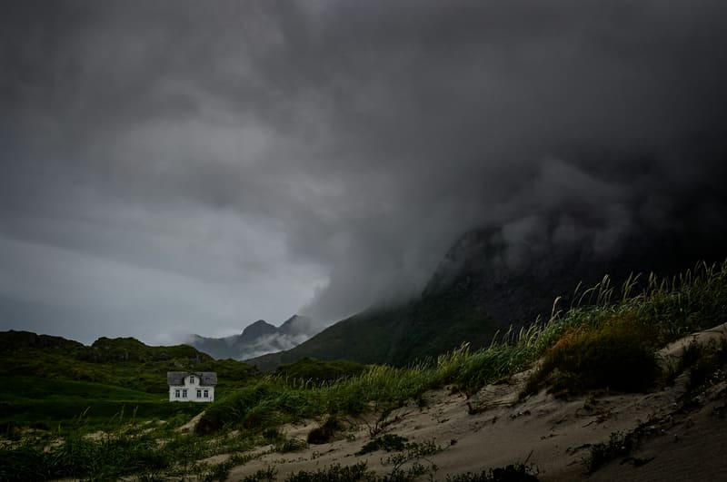 Small white house with mountains and storm clouds