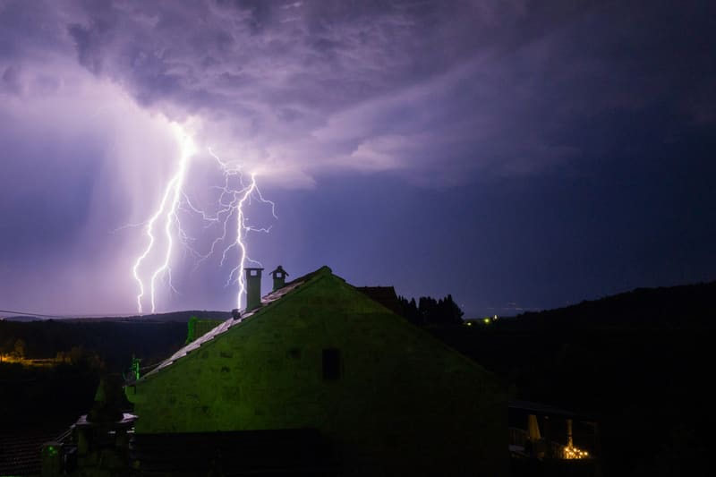 Lightning strike behind a house roof at night