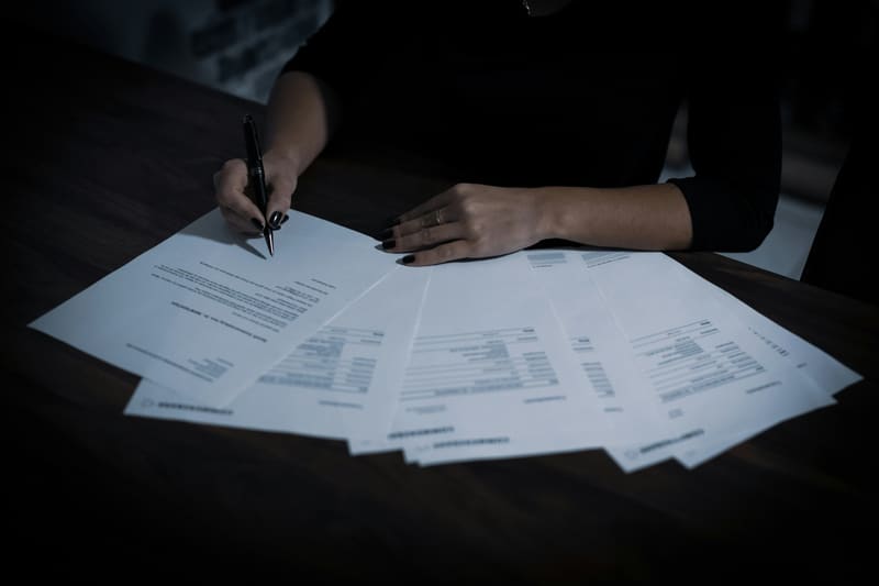Person signing documents at a dark desk