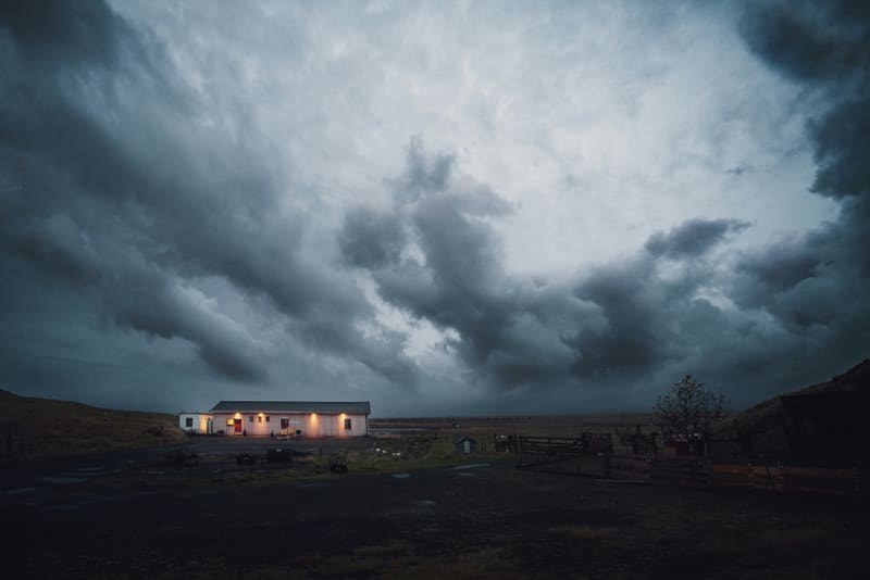Storm clouds gathering over a lit farmhouse at dusk