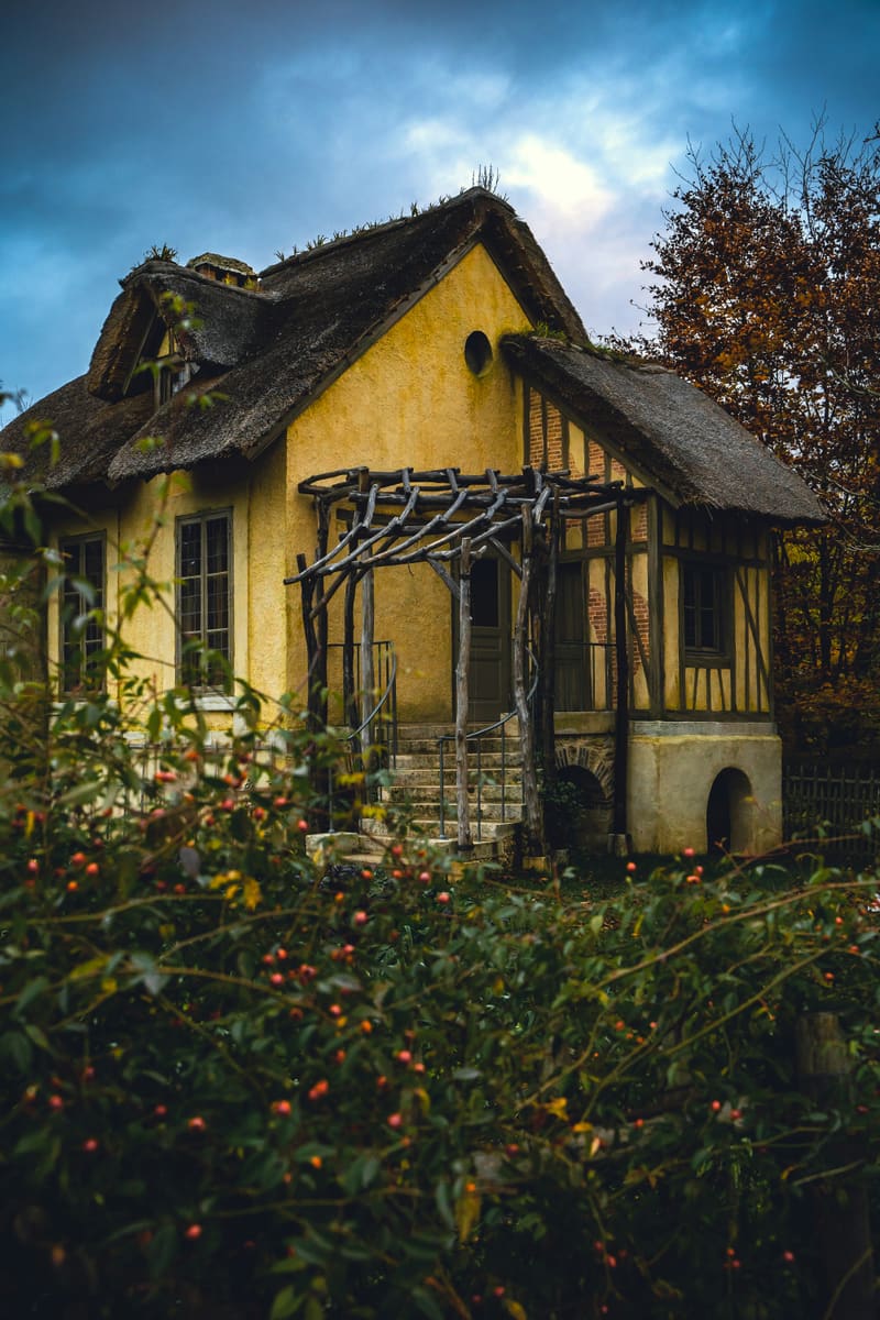 Yellow thatched-roof cottage under a stormy sky